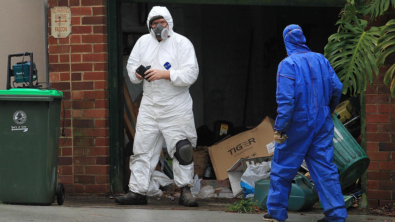 Cleaners and forensic police clear trash from the house where the rotting bodies of two dead men lay inside.